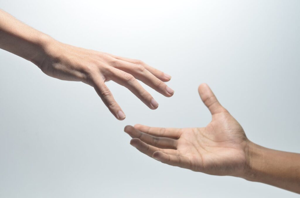 Close-up of two hands reaching towards each other on a neutral background, symbolizing connection.