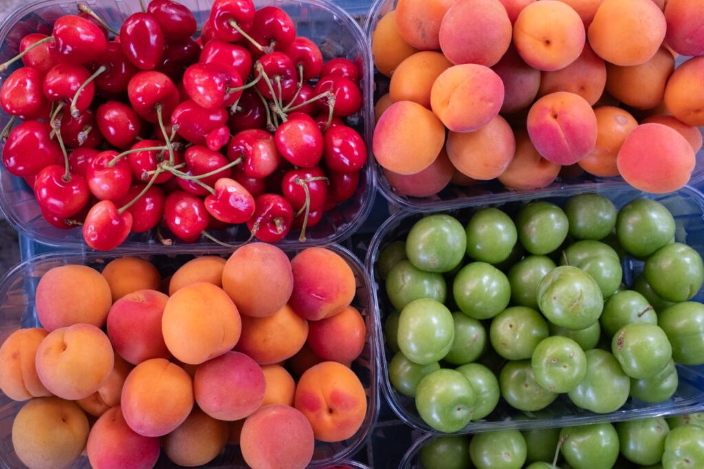 Top view of fresh cherries, apricots, and plums displayed in trays, showcasing vibrant colors.