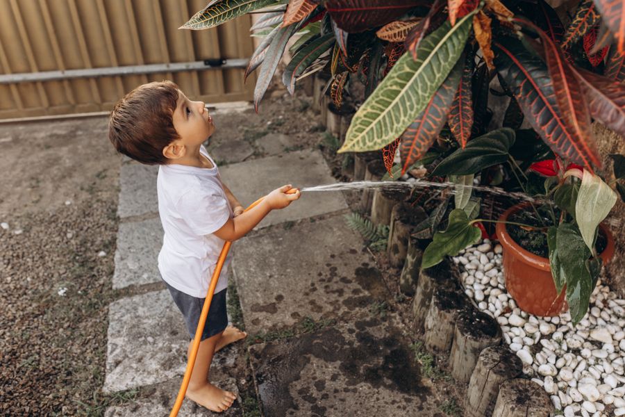 Criança regando plantas com uma mangueira em um dia ensolarado