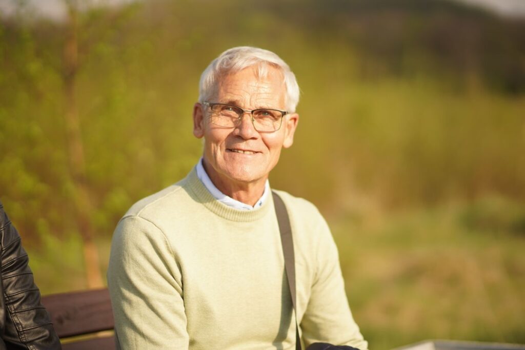 Senhor idoso sorrindo sentado ao ar livre sob a luz do sol